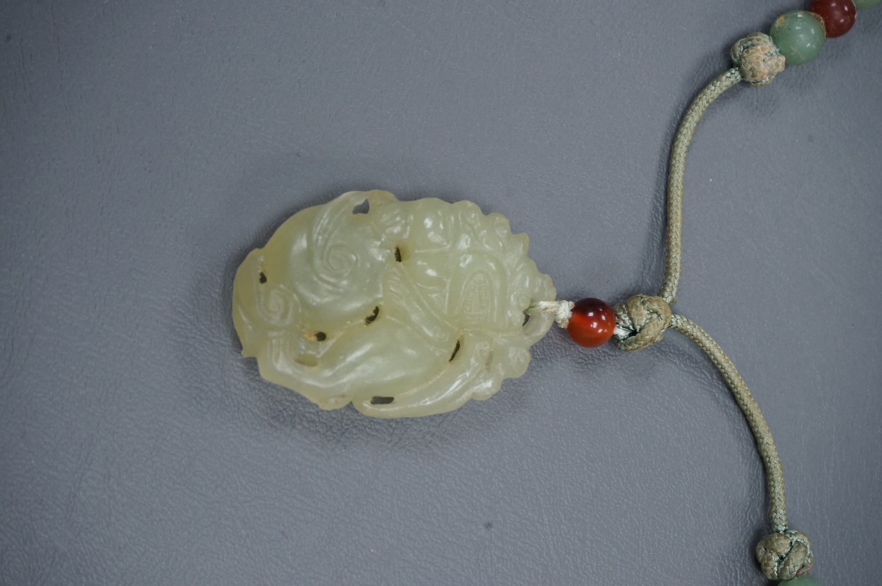 A Chinese carved bowenite jade pendant, on knotted beaded cord, pendant 6cm long.
